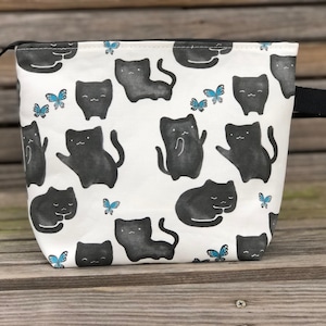 May include: White zippered pouch with a black and white cat and butterfly print. The pouch has a black handle.