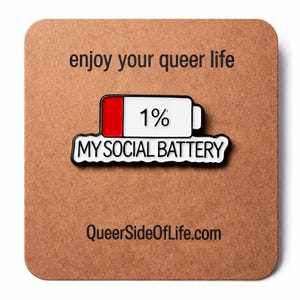 Könnte beinhalten: Eine weiß-rote Emaille-Anstecknadel in Form eines Akku-Symbols mit dem Text 1% MY SOCIAL BATTERY. Die Anstecknadel ist auf einer quadratischen braunen Karte befestigt, die oben mit enjoy your queer life und unten mit QueerSideOfLife.com bedruckt ist.