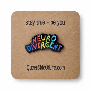 Könnte beinhalten: Eine schwarze Emaille-Anstecknadel mit dem Wort NEURODIVERGENT in bunten Buchstaben, befestigt auf einer braunen Karte mit dem in schwarzer Tinte gedruckten Text stay true - be you und QueerSideOfLife.com. Die Anstecknadel hat eine geschwungene Schrift.