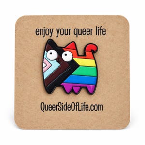 Könnte beinhalten: Eine katzenförmige Emaille-Anstecknadel in den Farben der Progress Pride Flagge, darunter Schwarz, Braun, Hellblau, Rosa, Weiß, Rot, Orange, Gelb, Grün, Blau und Violett. Die Anstecknadel ist auf einer beigen Karte mit dem Text enjoy your queer life und QueerSideOfLife.com befestigt.