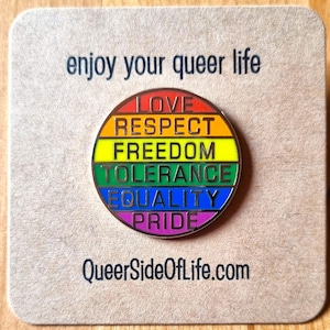 Könnte beinhalten: Ein runder, regenbogenfarbener Anstecker mit den Wörtern "LOVE, RESPECT, FREEDOM, TOLERANCE, EQUALITY, PRIDE" in vertikaler Anordnung. Der Anstecker befindet sich auf einer beigefarbenen Karte mit dem Text "enjoy your queer life" und "QueerSideOfLife.com".