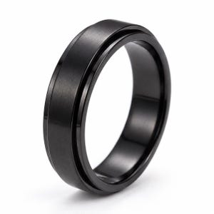 Op de afbeelding: Een massieve zwarte ring met een geborstelde matte afwerking op de centrale band, gecontrasteerd door gepolijste, glanzende randen. Het ontwerp bevat een duidelijke, dunne groef die horizontaal rond de omtrek van de band loopt.