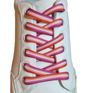 May include: Close-up of a white sneaker with colorful shoelaces. The shoelaces are a vibrant mix of pink, orange, and white stripes, creating a bold and eye-catching design. The laces are threaded through white eyelets.