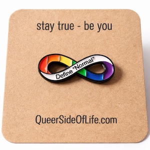 Puede incluir: Un pin con el símbolo del infinito de color arcoíris con las palabras "Define Normal" en una pancarta blanca. El pin está en una tarjeta marrón con el texto "stay true - be you" y "QueerSideOfLife.com".