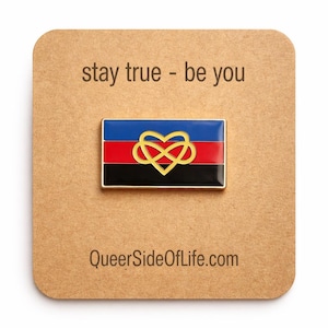 Puede incluir: Pin rectangular con borde dorado, con un diseño de bandera azul, roja y negra con un símbolo de infinito dorado en forma de corazón. El pin está sobre una tarjeta marrón con el texto "stay true - be you" y "QueerSideOfLife.com".