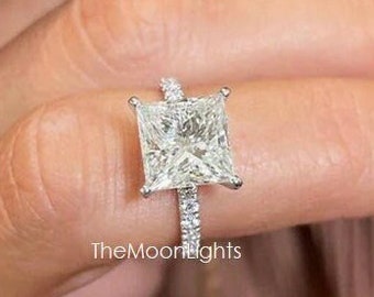 Könnte beinhalten: Ein quadratischer Diamantring mit Pavé-Fassung. Der Ring ist aus Weißgold gefertigt und hat einen großen, klaren Diamanten in der Mitte.