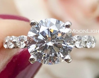 May include: A silver engagement ring with a large, round, clear center stone and smaller clear stones set in a pave band.