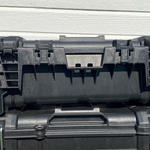 May include: Black plastic toolboxes stacked on top of each other. The top toolbox has the text "FIX & GO" printed on the side. The toolboxes have metal latches and handles.