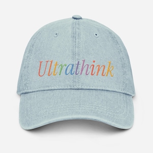 Peut inclure: Casquette de baseball en jean bleu clair avec le mot "Ultrathink" brodé en couleurs arc-en-ciel. La casquette a une visière incurvée et une sangle réglable à l'arrière. Un accessoire décontracté.