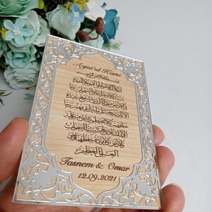 May include: A wooden plaque with a silver border and intricate floral designs. The plaque features an Arabic inscription, the text "Ayatul Kurei", and the names "Tasnem & Omar" with the date "12.09.2021".