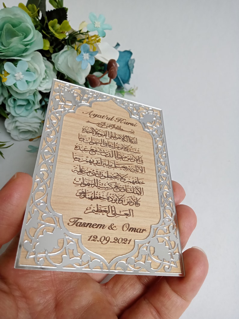 May include: A wooden plaque with a silver border and intricate floral designs. The plaque features an Arabic inscription, the text "Ayatul Kurei", and the names "Tasnem & Omar" with the date "12.09.2021".