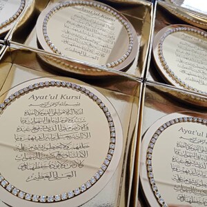 May include: Gold-colored round coasters with a decorative border of rhinestones. The center of each coaster features a gold-colored inscription of the Arabic text "Ayat'ul Kursi" in a decorative font.