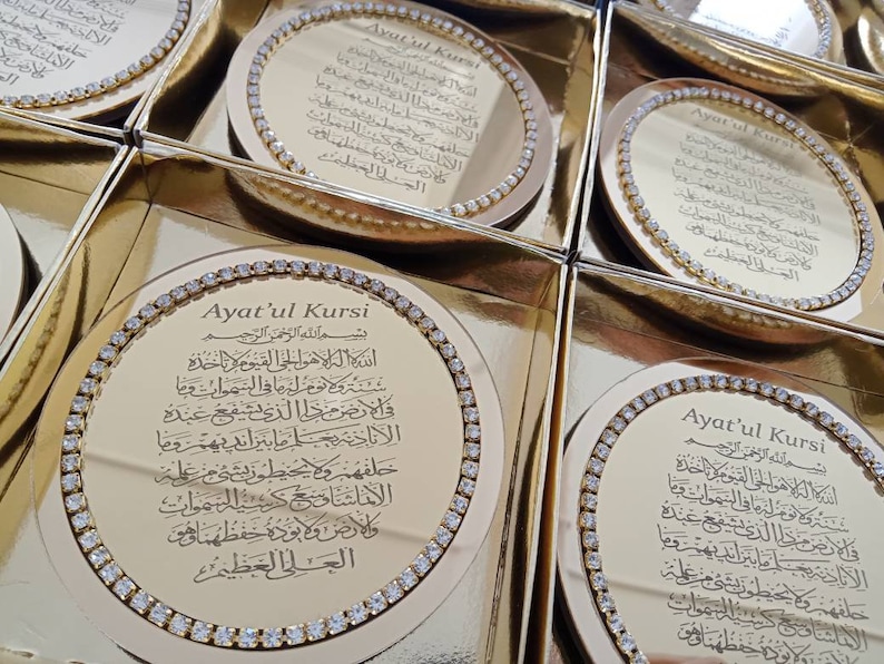 May include: Gold-colored round coasters with a decorative border of rhinestones. The center of each coaster features a gold-colored inscription of the Arabic text "Ayat'ul Kursi" in a decorative font.