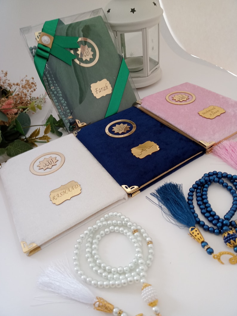 May include: A collection of four velvet-covered books in white, navy blue, pink, and green, each featuring gold-toned corner protectors, a circular emblem with Arabic calligraphy, and a personalised name plaque. Two sets of prayer beads are included.