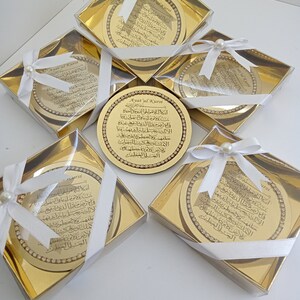 May include: Five gold-colored gift boxes with white ribbon and pearl accents. Each box contains a round, gold-colored plaque with Arabic calligraphy and the text "Ayatul Kursi" in English.