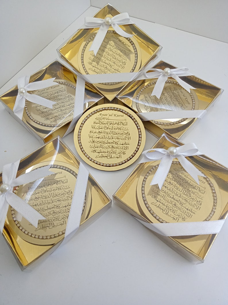 May include: Five gold-colored gift boxes with white ribbon and pearl accents. Each box contains a round, gold-colored plaque with Arabic calligraphy and the text "Ayatul Kursi" in English.