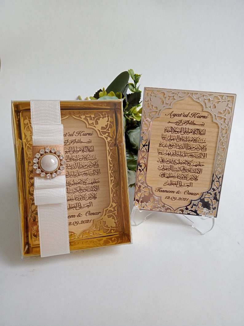 May include: Two wooden plaques with gold-colored trim and Arabic calligraphy. The plaques are engraved with the text "Ayatul Kursi" and "Bismillah ar-Rahman ar-Rahim". The plaques are on a white background.
