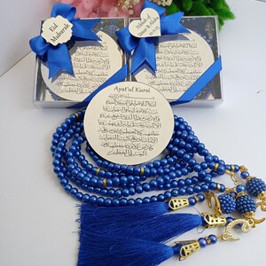 Op de afbeelding: Een blauwe en gouden islamitische gebedsstreng met een zilveren plaquette met de Ayatul Kursi-vers. De plaquette zit in een zilveren doos met een blauw lint en een hartvormig label met de tekst "Nikkah of Umar & Alisha 10.11.23".