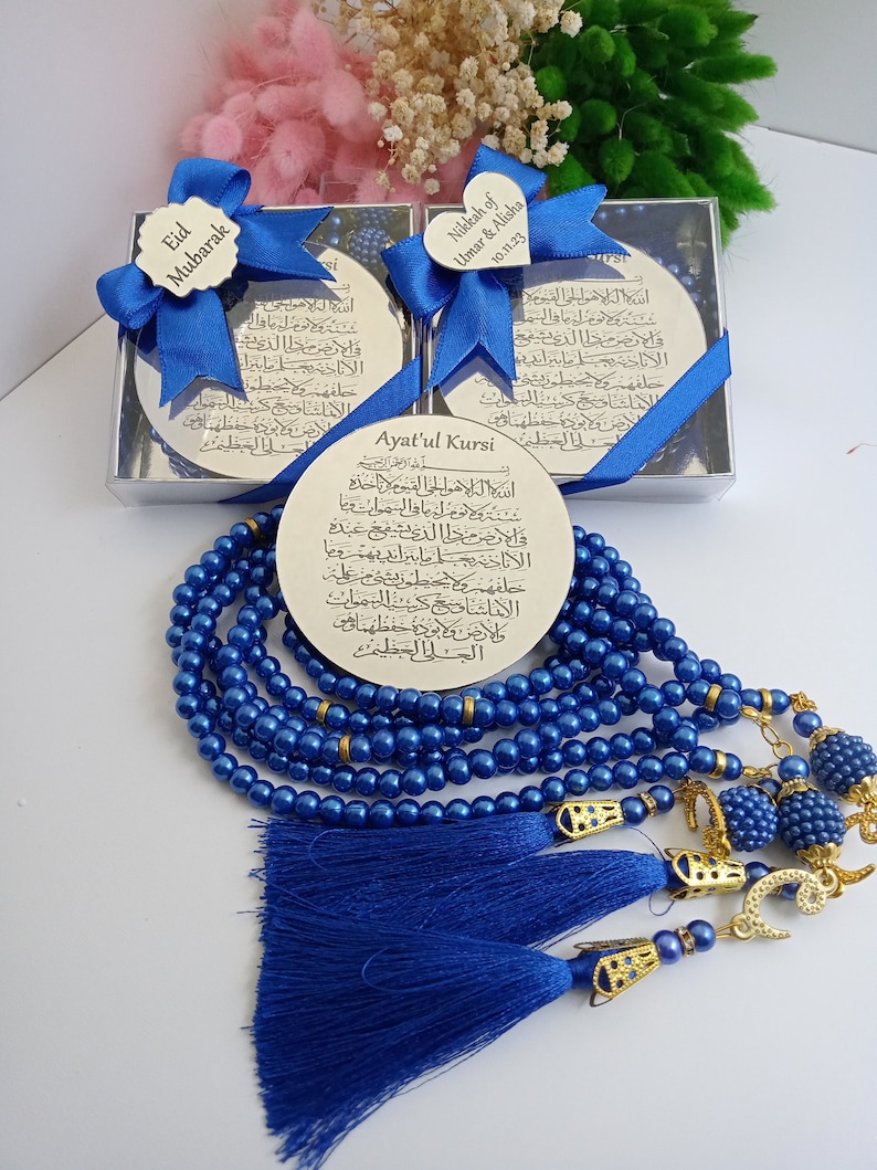 Op de afbeelding: Een blauwe en gouden islamitische gebedsstreng met een zilveren plaquette met de Ayatul Kursi-vers. De plaquette zit in een zilveren doos met een blauw lint en een hartvormig label met de tekst "Nikkah of Umar & Alisha 10.11.23".
