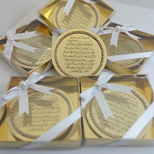 May include: Gold-colored decorative round boxes with white ribbon and pearl accents. Each box contains a gold-colored round plaque with Arabic calligraphy and the text "Ayatul Kursi".