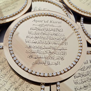 May include: A gold-colored round mirror with a decorative border of rhinestones. The mirror features an inscription in Arabic script, "Ayat'ul Kursi", which is a verse from the Quran.
