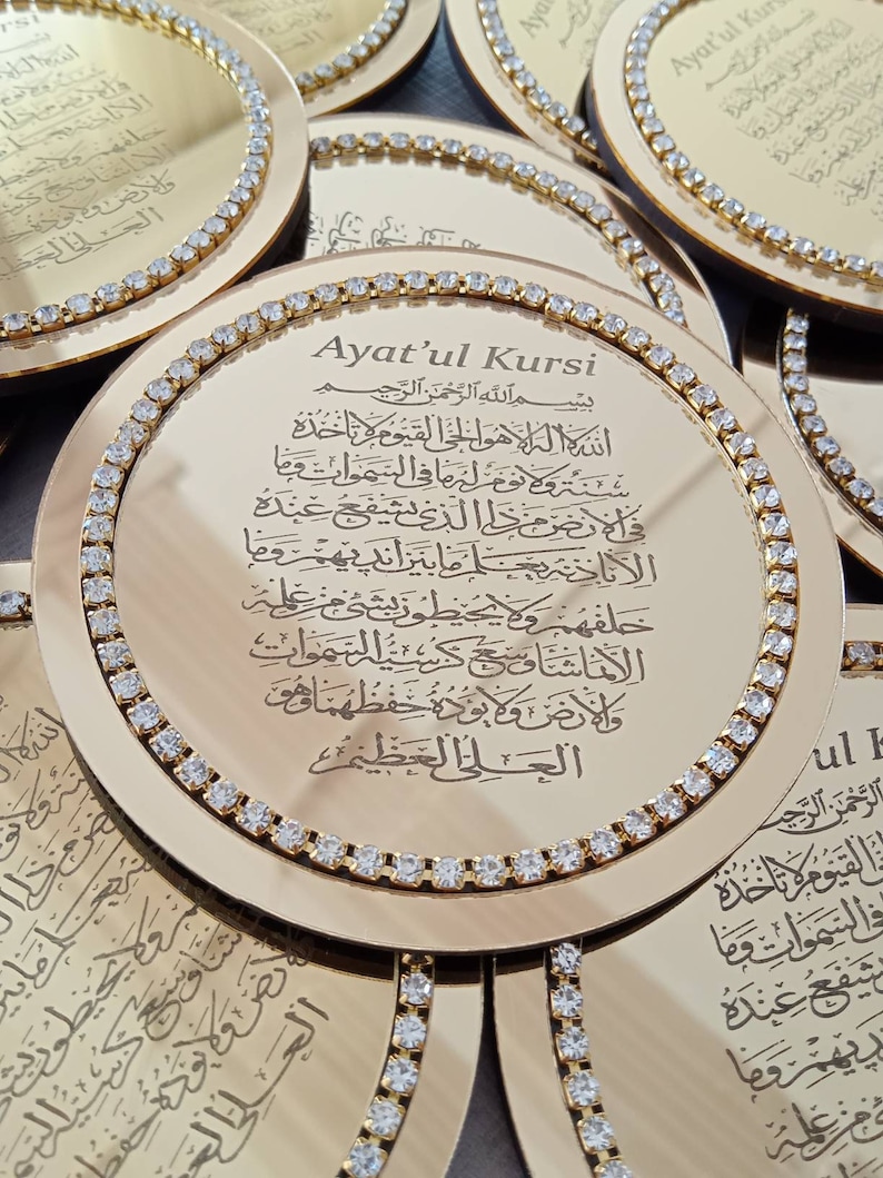 May include: A gold-colored round mirror with a decorative border of rhinestones. The mirror features an inscription in Arabic script, "Ayat'ul Kursi", which is a verse from the Quran.