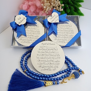 Op de afbeelding: Een blauwe gebedsketting met een gouden kwast en een zilveren bedel met Arabische schrift. De ketting wordt gepresenteerd met een zilveren doos die een zilveren plaquette met Arabische schrift en de tekst "Ayat'ul Kursi" bevat.