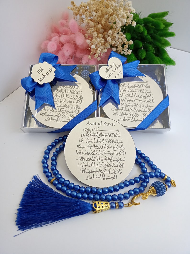 Op de afbeelding: Een blauwe gebedsketting met een gouden kwast en een zilveren bedel met Arabische schrift. De ketting wordt gepresenteerd met een zilveren doos die een zilveren plaquette met Arabische schrift en de tekst "Ayat'ul Kursi" bevat.