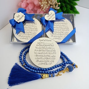 Op de afbeelding: Een blauwe en gouden gebedsparelset met een zilveren ronde plaquette gegraveerd met Arabische schrift en de woorden "Ayat'ul Kursi". De plaquette bevindt zich in een doorzichtige doos met een blauw lint en een hartvormig label met de tekst "Nikkah of Umar & Alisha 10.11.23".
