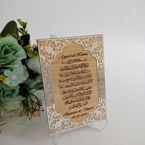 May include: A wooden plaque with a silver frame and intricate floral designs. The plaque features the Arabic text of Ayatul Kursi, a verse from the Quran, and the names "Fasnem & Omar" with the date "12.09.2021".