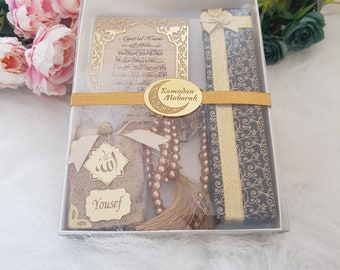 Könnte beinhalten: Eine weiße Geschenkbox mit einer goldgerahmten Ayat al-Kursi-Plakette, einer dunkelblauen Box mit goldenem Band, einem beigen Stoffbeutel mit dem Namen Yousef und arabischer Kalligrafie sowie einer goldenen Gebetskette mit Ramadan Mubarak-Anhänger.