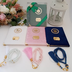 May include: Three velvet-covered books in white, pink, and navy blue, each featuring a gold circular emblem with Arabic script and a personalised gold nameplate. Three matching pearl-bead prayer beads with tassels accompany the books.