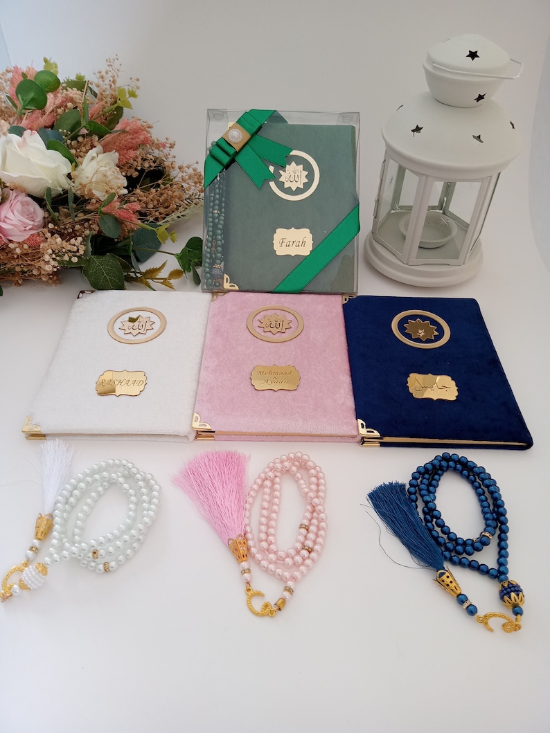 May include: Three velvet-covered books in white, pink, and navy blue, each featuring a gold circular emblem with Arabic script and a personalised gold nameplate. Three matching pearl-bead prayer beads with tassels accompany the books.