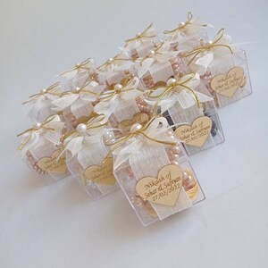 May include: A collection of small, clear boxes tied with white ribbon and gold string. Each box contains a small heart-shaped wooden tag with the text "Nikaah of Sehar & Sufiyan 27/02/2022".