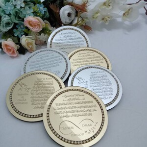 May include: A set of five gold and silver round decorative plaques with a diamond-like border. The plaques feature the Arabic text "Ayat'ul Kursi" and the names "Tasnem" and "Omar" with the date "12.09.2021".