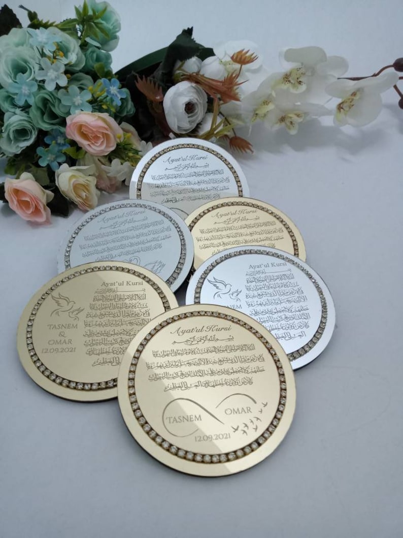 May include: A set of five gold and silver round decorative plaques with a diamond-like border. The plaques feature the Arabic text "Ayat'ul Kursi" and the names "Tasnem" and "Omar" with the date "12.09.2021".