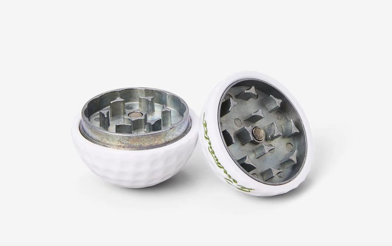 May include: Two white golf ball shaped grinders with a silver metal grinding mechanism. The grinders have a green logo that says "Swingers" on them.