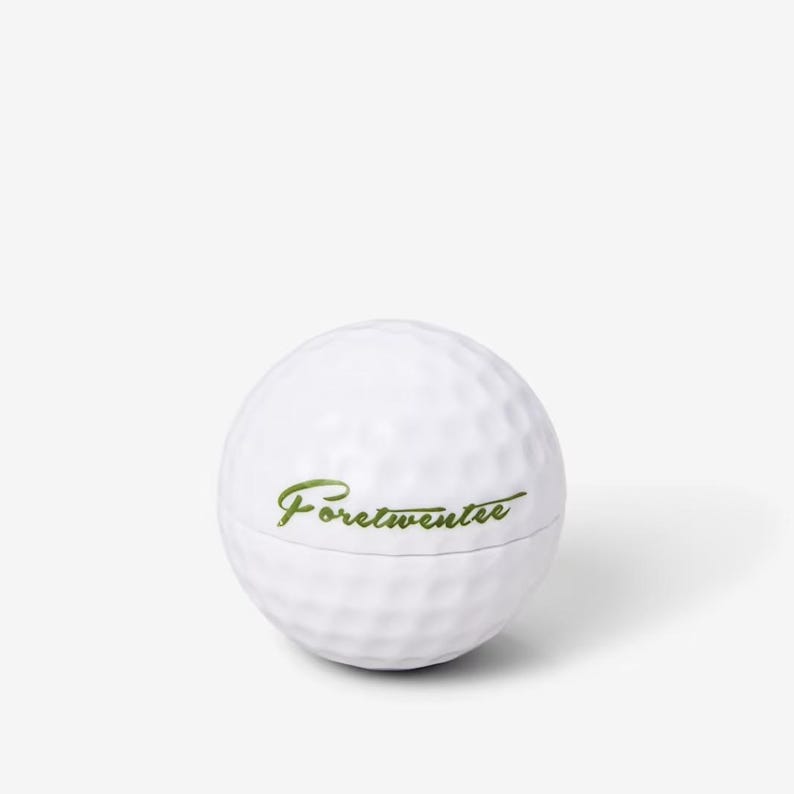 May include: White golf ball with the text "Fore!twenteee" in green lettering.