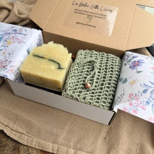 May include: A gift box containing a bar of soap, a green washcloth, and floral-printed wrapping paper. The soap is light green with a dark green swirl and a small floral design. The box has the text "La Dolce Ulla Living".