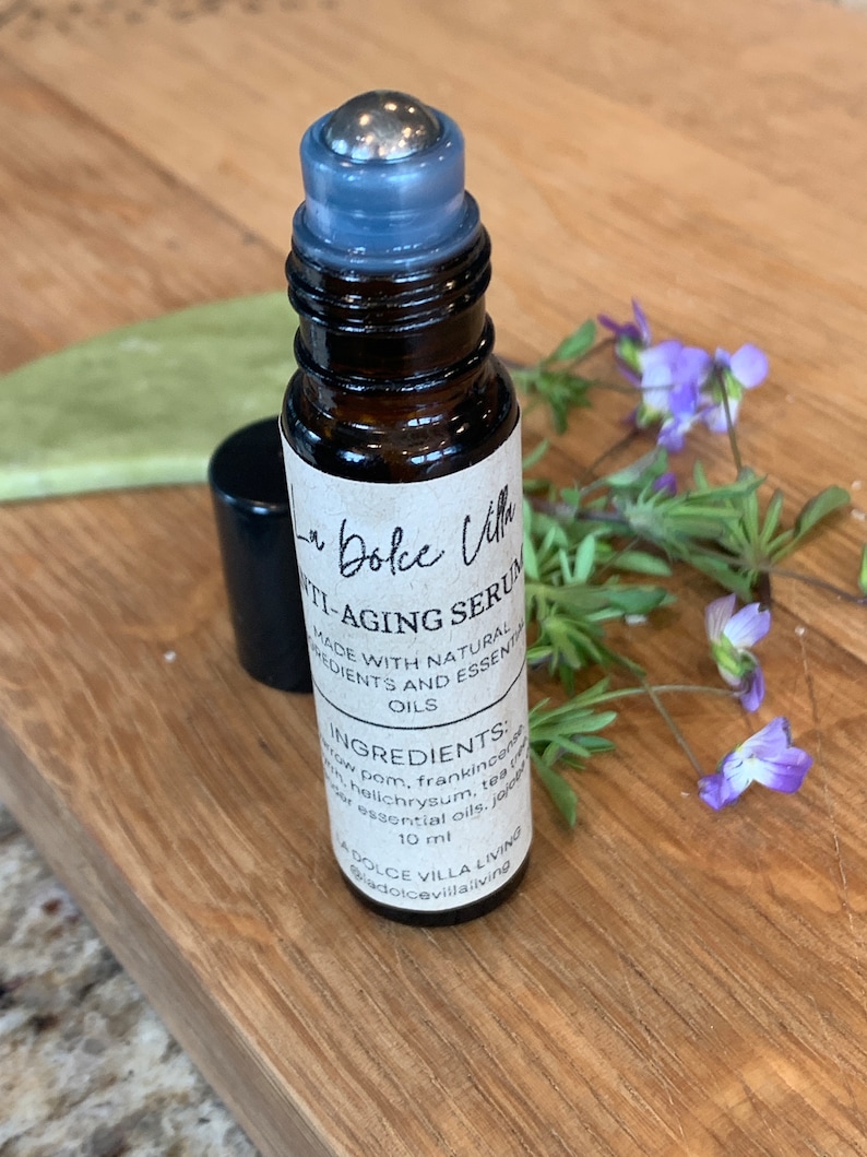 Puede incluir: Un frasco de vidrio marr&oacute;n con una bola de rodillo plateada en la parte superior. El frasco est&aacute; etiquetado como "La Dolce Villa Anti-Aging Serum" y enumera los ingredientes: "Incienso, Helichrysum, &Aacute;rbol de T&eacute;, Aceites Esenciales de Jojoba". El frasco contiene 10 ml de suero.
