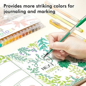 May include: A set of 24 colourful gel pens in a clear plastic case with a pink bow. The pens are arranged in rows and are labelled "colours". The text "Part 4" is visible on the case. A hand is holding a green gel pen and writing in a journal with a floral design.
