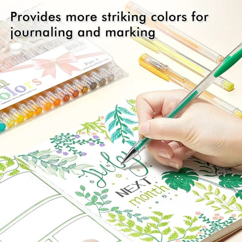 May include: A set of 24 colourful gel pens in a clear plastic case with a pink bow. The pens are arranged in rows and are labelled "colours". The text "Part 4" is visible on the case. A hand is holding a green gel pen and writing in a journal with a floral design.