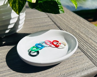 May include: A white ceramic dish with eight silicone rings in various colors, including black, green, blue, light blue, pink, red, and white. The rings are arranged in a semi-circle on the dish.