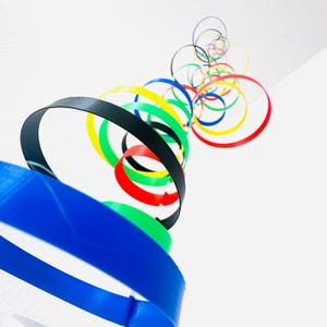 May include: A colorful mobile made of interlocking rings in the colors of the Olympic rings: blue, yellow, black, green, and red. The rings are suspended from the ceiling and are arranged in a spiral pattern.