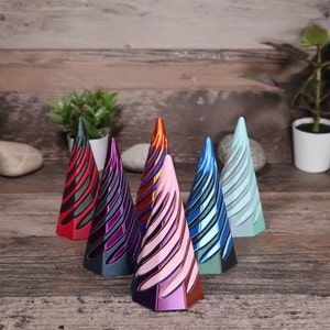 May include: Six decorative, metallic, cone-shaped ornaments in various colors, including red, purple, pink, orange, blue, and teal. The ornaments are arranged in a row on a wooden surface.