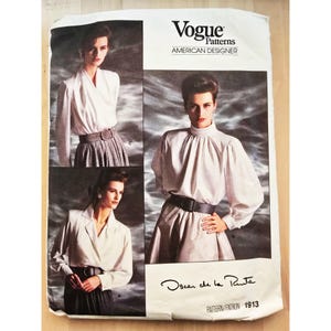 May include: A Vogue Patterns American Designer sewing pattern envelope for Oscar de la Renta design 1913. The white paper envelope features three photographs of a model wearing long-sleeved white blouses with high or lapel collars and belts.