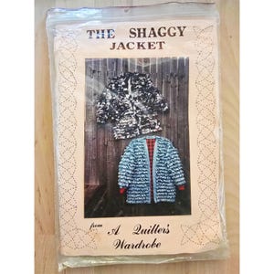 May include: A sewing pattern titled "The Shaggy Jacket" from "A Quilter's Wardrobe." The pattern shows two examples of the jacket: one in black and white, and another in blue with a red and black plaid lining. The pattern is in a clear plastic bag.