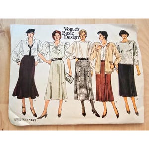 May include: A vintage Vogue's Basic Design sewing pattern featuring illustrations of five different women's outfits. The outfits include blouses, skirts, and a cardigan. The pattern is labeled "Pattern 1425".
