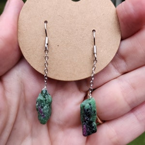 May include: A pair of green and pink gemstone earrings with silver chains and hooks.