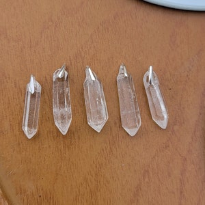 May include: Five clear quartz crystal pendants with silver jump rings. The pendants are all different sizes and shapes, but they are all clear and have a natural, raw look.
